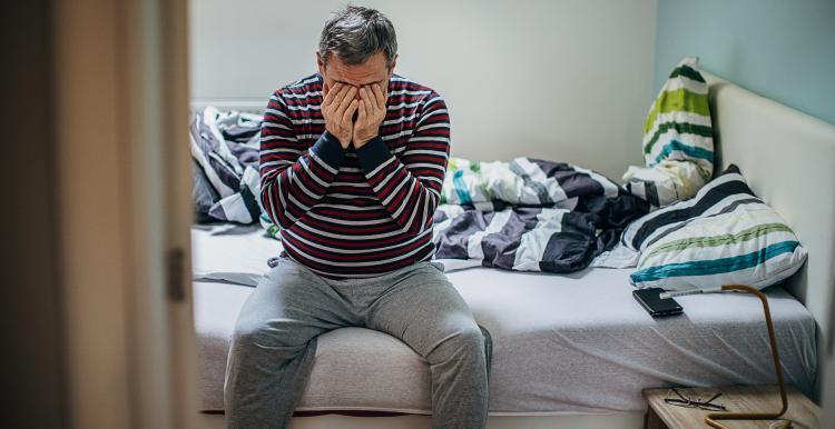 Man sat on edge of bed holding hands over face